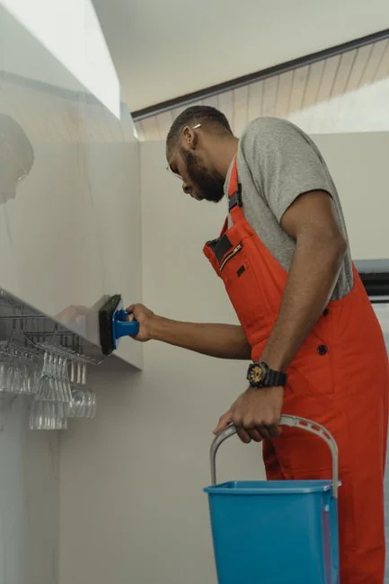 gallery-01 A man wearing a blue t-shirt cleaning a large glass pane indoors with a squeegee.